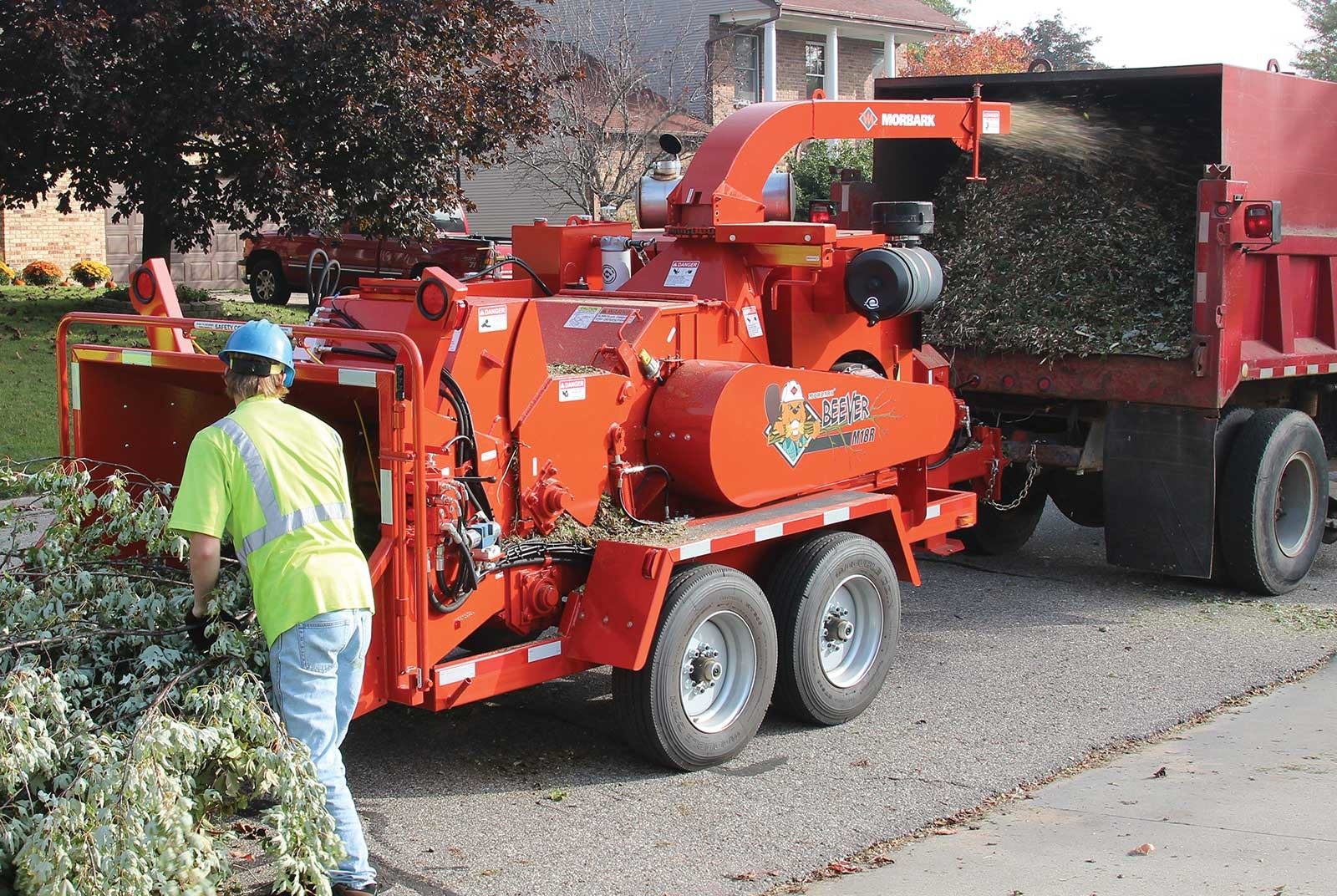 A worker in hi-vis gear beside a red wood chipper on a job